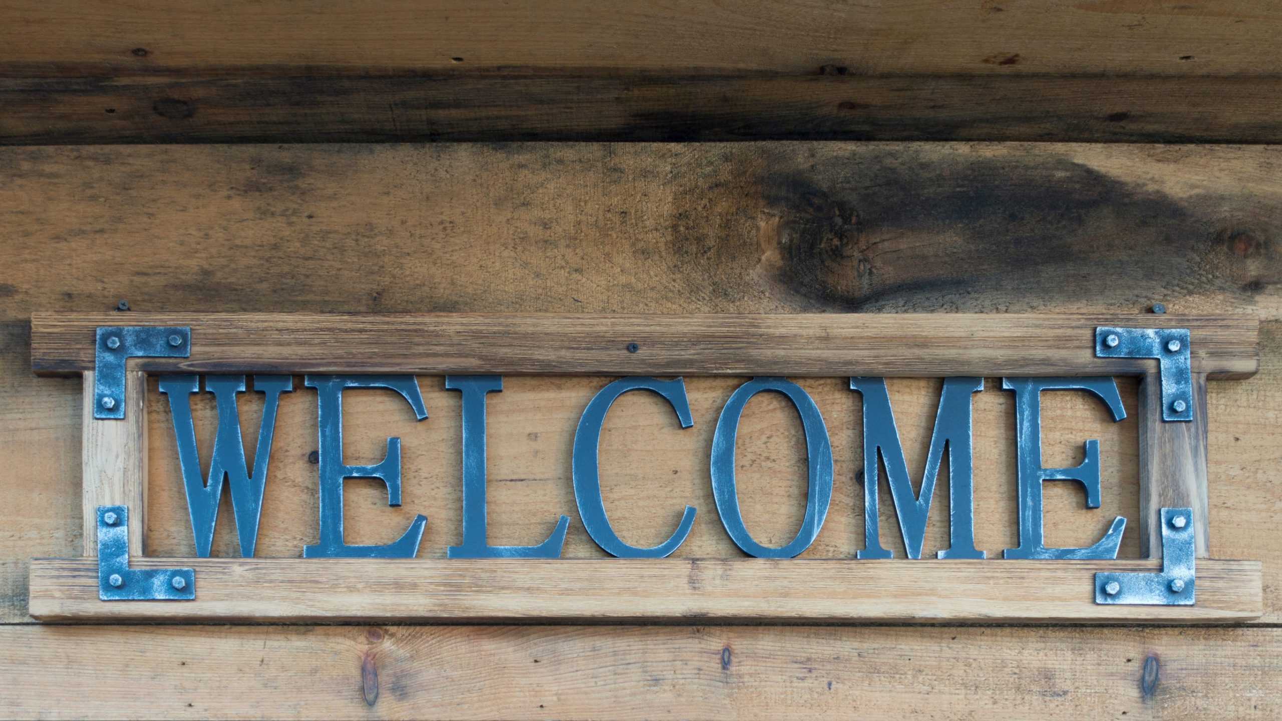 A wooden sign with metal letters spelling "WELCOME" is mounted on a wooden wall, inviting guests to explore Year-Round Activities Aitkin has to offer.