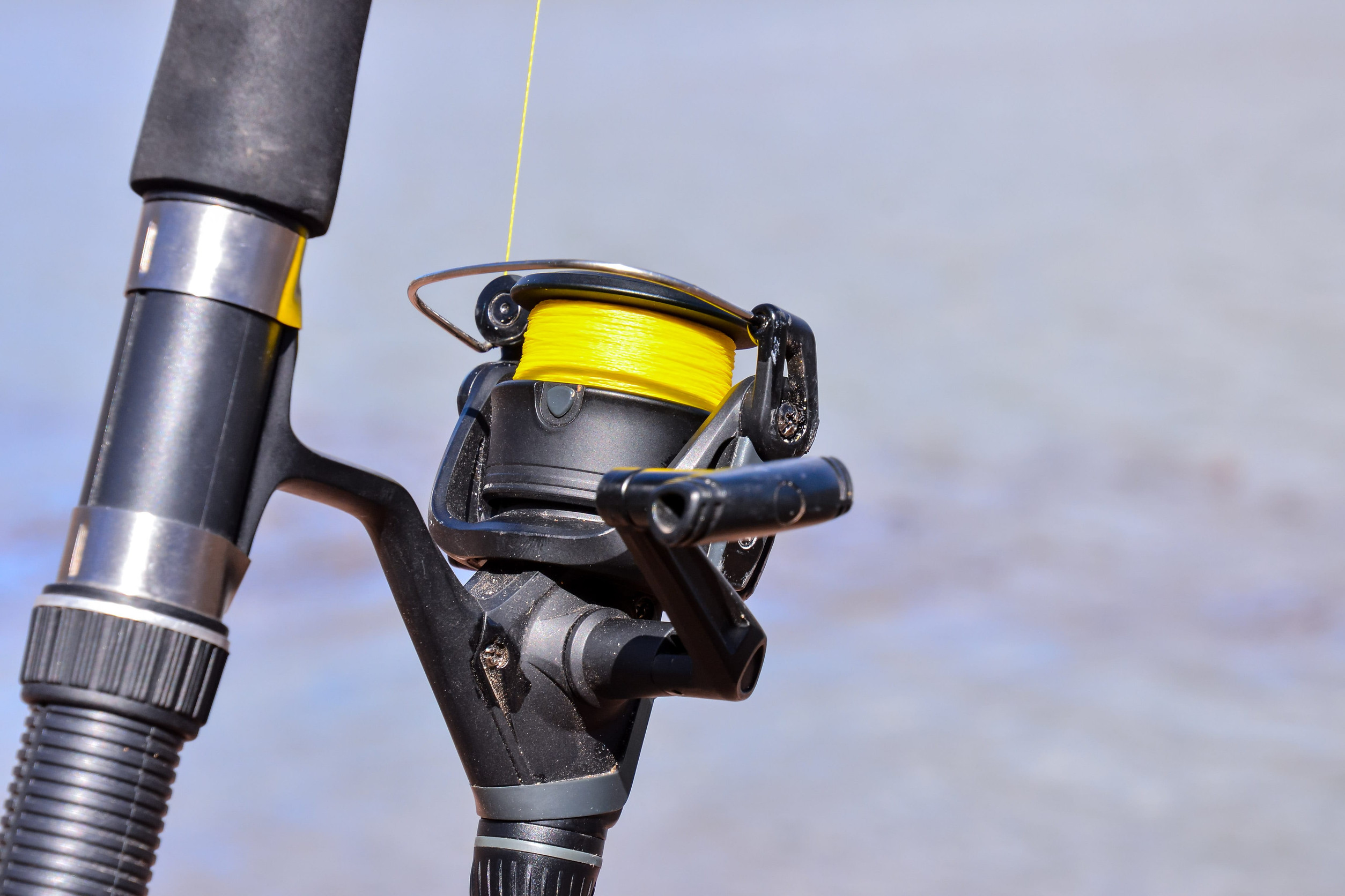 Close-up of a fishing reel with bright yellow line on a black rod, set against a blurred outdoor background—perfect for the excitement of the Minnesota Fishing Opener near Aitkin.